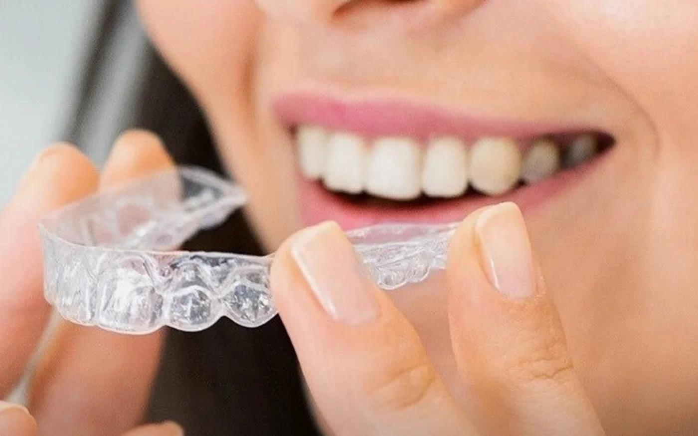 A smiling person holding a clear aligner